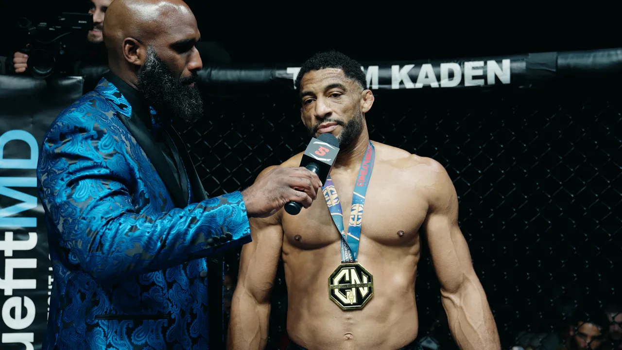 Julien Williams with the medal, speaking on the microphone in the cage