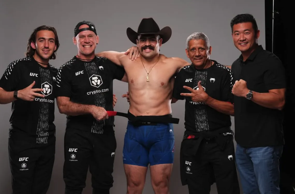 Luis Hernandez backstage in a cowboy hat with his team, a black belt around his waist